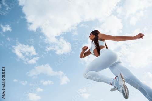 Up in the sky. Female runner in white sportive clothes doing fitness