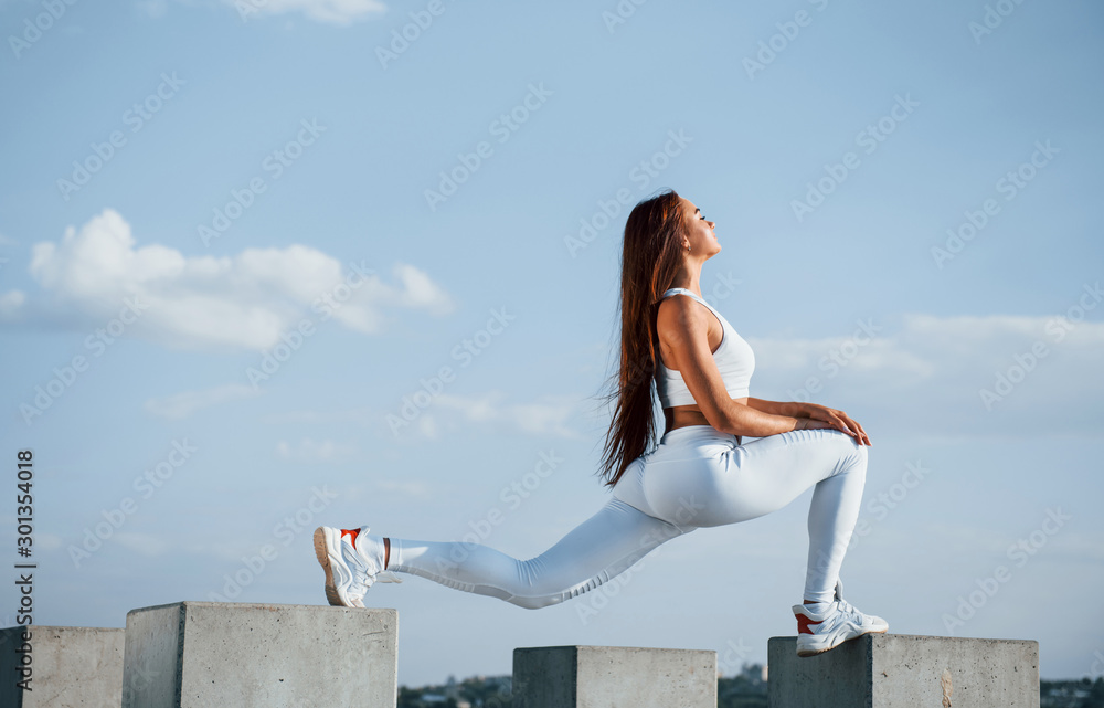 Standing on the cement cube. Shot of sportive woman doing fitness exercises near the lake at daytime Standing on the cement cube. Shot of sportive woman doing fitness exercises near the lake at daytime