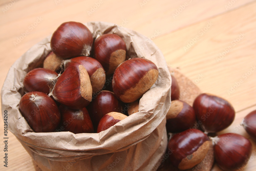 Bunch of ripe chestnuts in a paper bag on wooden background on selective focus Bunch of ripe chestnuts in a paper bag on wooden background on selective focus