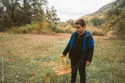 A boy walks through the meadow picking mushrooms.
