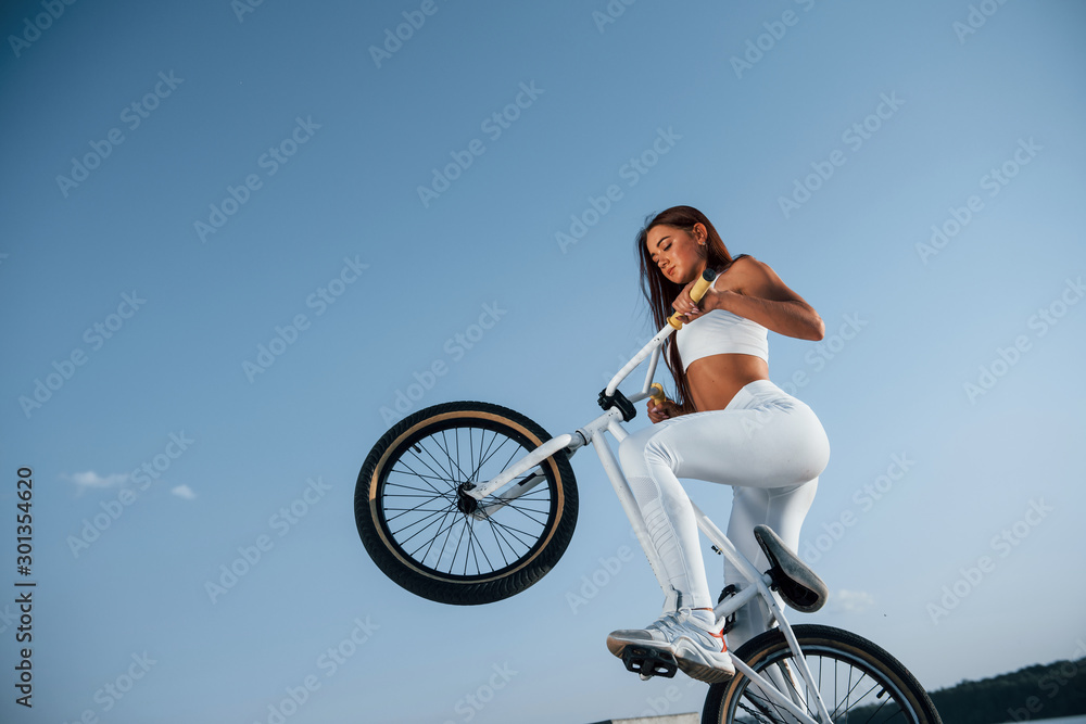 Photo in motion. Doing stunts. Female rider is on the bike at daytime near the lake. Fitness woman in sportive clothes