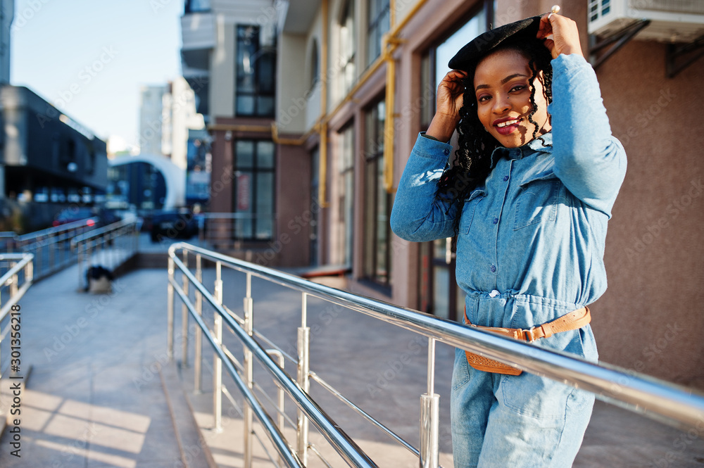 Stylish fashionable african american women in jeans wear and black beret against modern building.