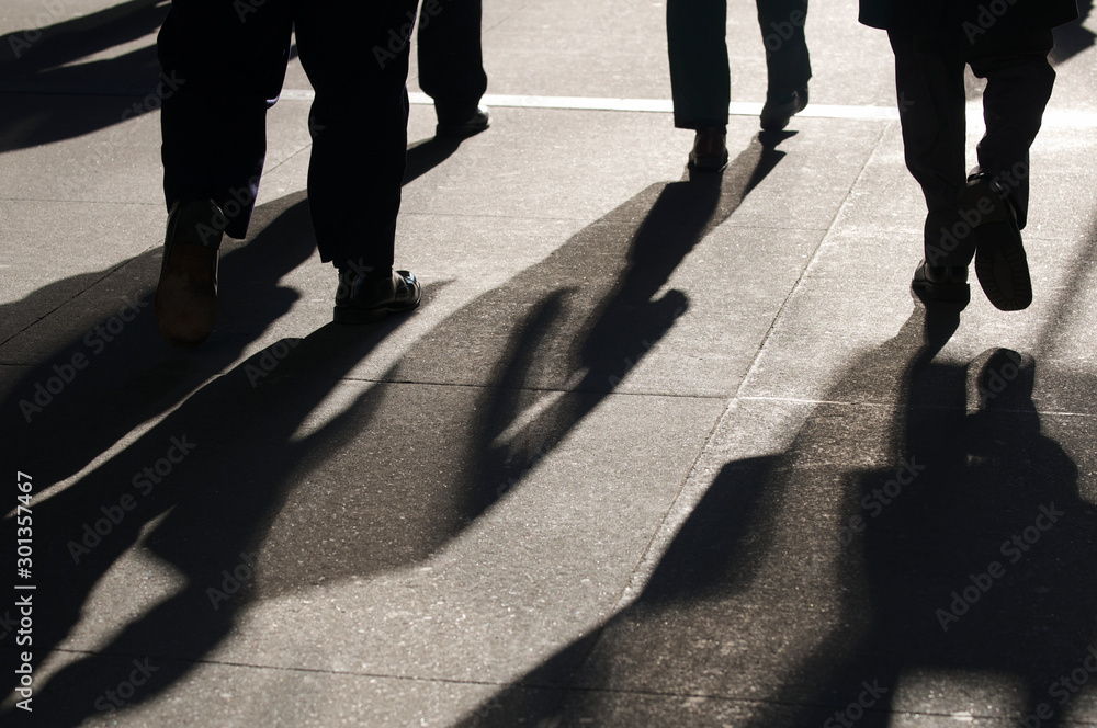 Morning sun casting dramatic shadows on the sidewalk behind silhouettes of commuting business people rushing to work Morning sun casting dramatic shadows on the sidewalk behind silhouettes of commuting business people rushing to work