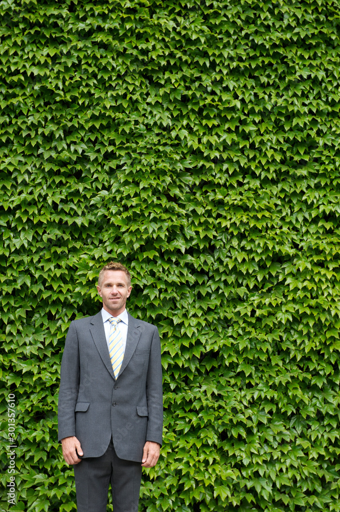 Portrait of businessman standing outdoors in front of a wall of bright green ivy copy space Portrait of businessman standing outdoors in front of a wall of bright green ivy copy space