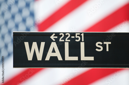 Close up of a Wall Street sign in New York City with American flag in the background