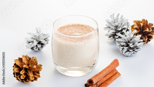Traditional Christmas cocktail Eggnog with eggs, alcohol, grated nutmeg and cinnamon closeup, copy space, vertical frame. Sweet traditional drink on grey table with beige decorations and pine cones