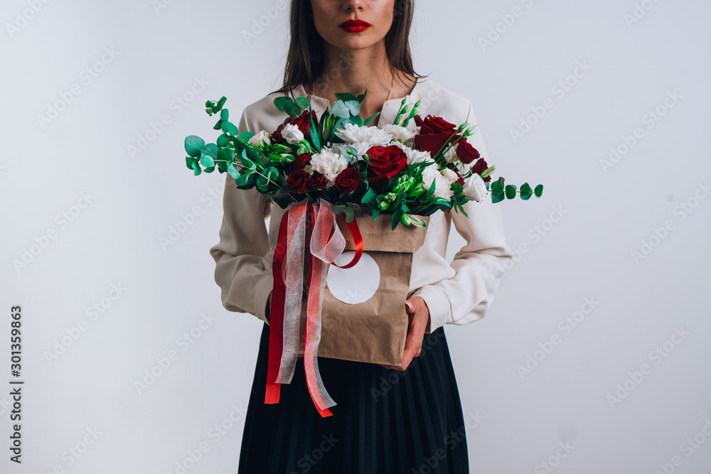 The girl holds in her hands a bouquet of flowers in a package. against the background of a gray wall. The image of a young teacher. The girl holds in her hands a bouquet of flowers in a package. against the background of a gray wall. The image of a young teacher.