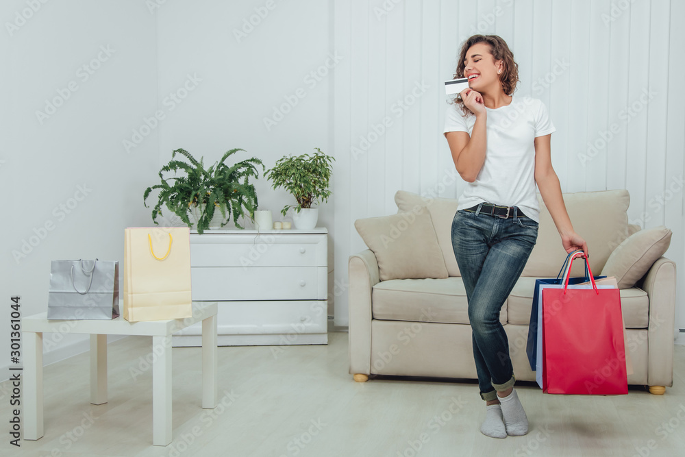 Cheerful kinky girl with shining smile is standing, holding four colorful shop bags in one hand and credit card close to face in another. Cheerful kinky girl with shining smile is standing, holding four colorful shop bags in one hand and credit card close to face in another.