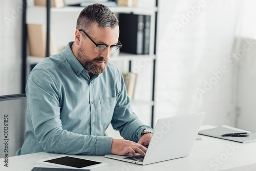 handsome businessman in shirt and glasses using laptop in office