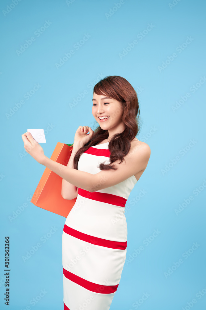 Pretty smiling Asian woman with shopping bags showing credit card in hand studio shot isolated on blue background Pretty smiling Asian woman with shopping bags showing credit card in hand studio shot isolated on blue background