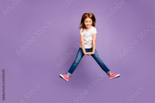 Full body photo of funny small ginger lady jumping high rejoicing in air cheerful crazy mood overjoyed weekend wear casual t-shirt jeans isolated purple background