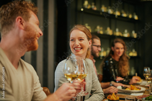 Couple sitting in restaurant with their friends and toasting with wine.