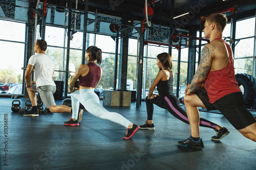 A group of muscular athletes doing workout at the gym. Gymnastics, training, fitness workout flexibility. Active and healthy lifestyle, youth, bodybuilding. Training in lunges and stretching exercises