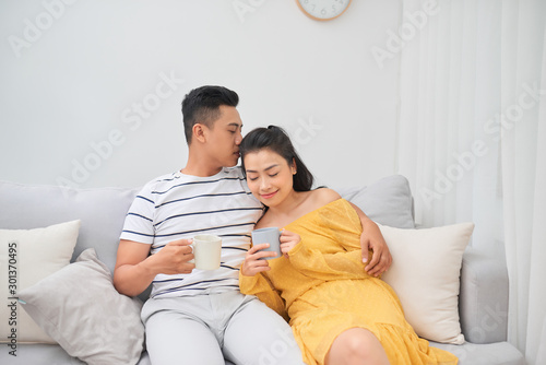 Affectionate couple holding coffee cups sitting on a sofa in the living room at home