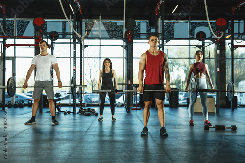 A group of muscular athletes doing workout at the gym. Gymnastics, training, fitness workout flexibility. Active and healthy lifestyle, youth, bodybuilding. Training with weights, doing squats.