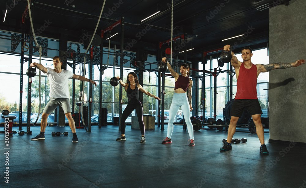 Fototapeta premium A group of muscular athletes doing workout at the gym. Gymnastics, training, fitness workout flexibility. Active and healthy lifestyle, youth, bodybuilding. Training with weights, doing squats.