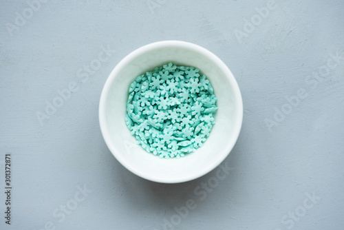 Turquoise Sprinkling snowflakes. Sugar sprinkles. Decoration for cake on gray wooden background. Christmas cooking. Christmas or New Year celebration concept.