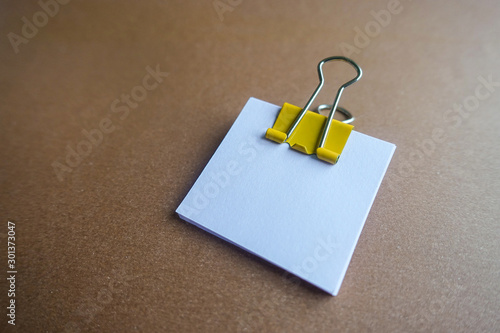 Yellow paper clip and blank paper on a brown background