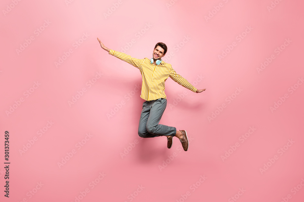 Full length photo of handsome guy jumping high enjoy summer time using earflaps flying like bird wear hipster striped shirt trousers isolated pink color background