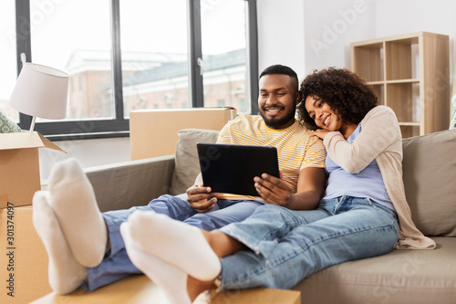 mortgage, people and real estate concept - happy african american couple with tablet pc computer sitting on sofa at new home