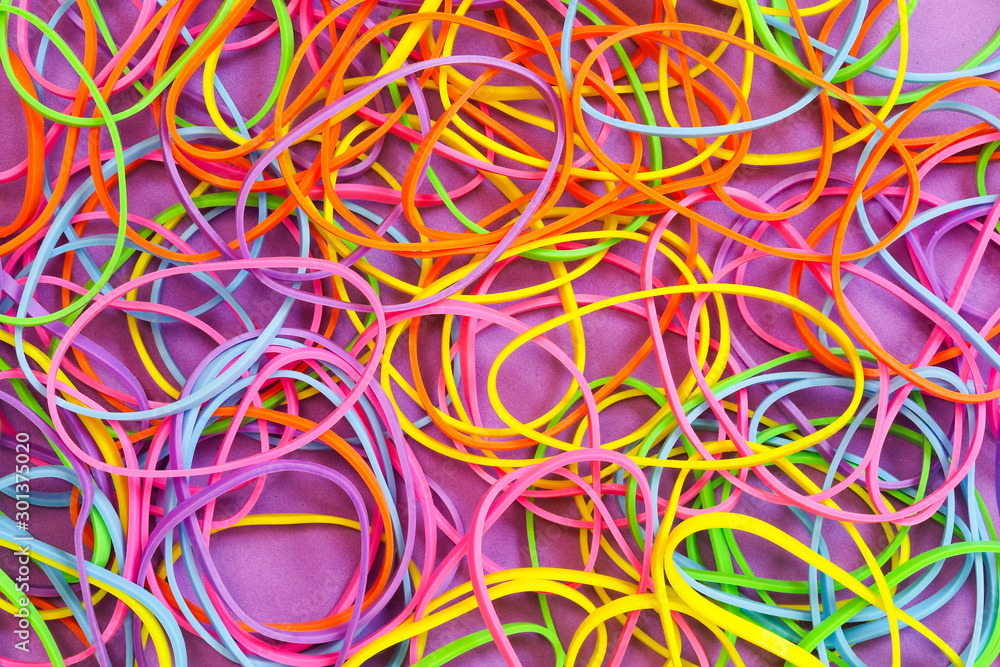 A pile of neon colored elastic rubber bands against a purple background