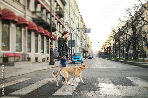 Young woman with dog on leash walking on pedestrian crossing