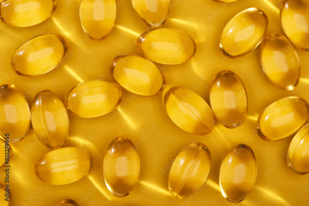 top view of golden shiny fish oil capsules scattered on yellow bright background top view of golden shiny fish oil capsules scattered on yellow bright background
