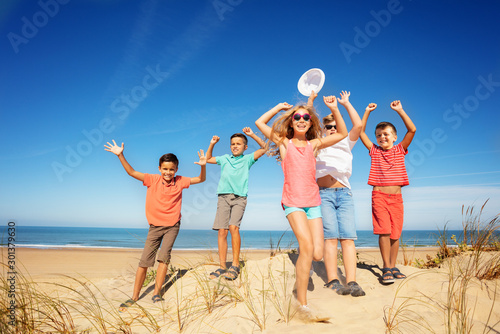 Happy group of kids jump lifting hands on the sand © Sergey Novikov