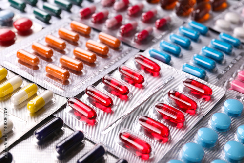 Flat lay composition with bunch of different colorful pills in blister packs. Pile of unopened medication on paper textured background. Close up, copy space.