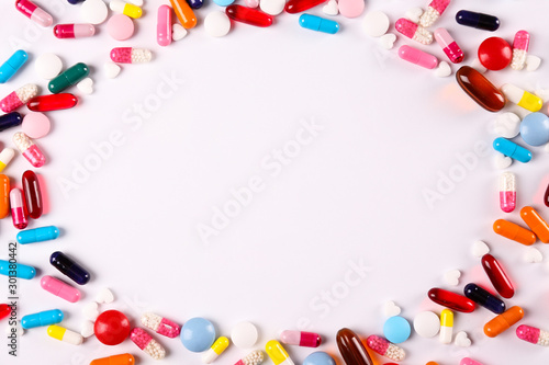 Flat lay composition with bunch of different colorful pills in scattered all over the table. Pile of opened medication on paper textured background. Close up, copy space.