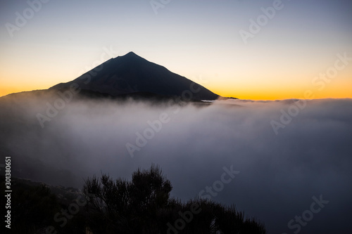 Sunset at the teide vulcan tenerife mountain with high clouds and top of the peak - orange sunlight in background - concept of scenery and beauty outdoor nature in national park
