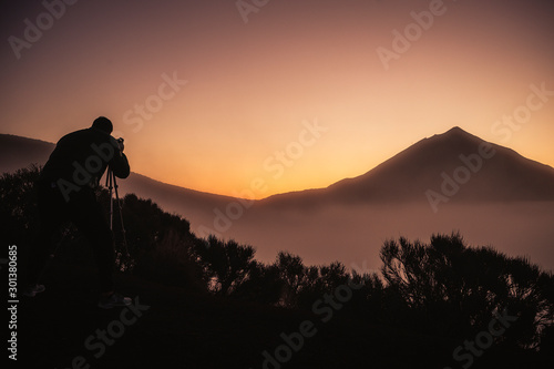 Photographer in action in scenery sunset with high mountain in background and orange colors around -wild active people enjoyin the outdoors leisure activity