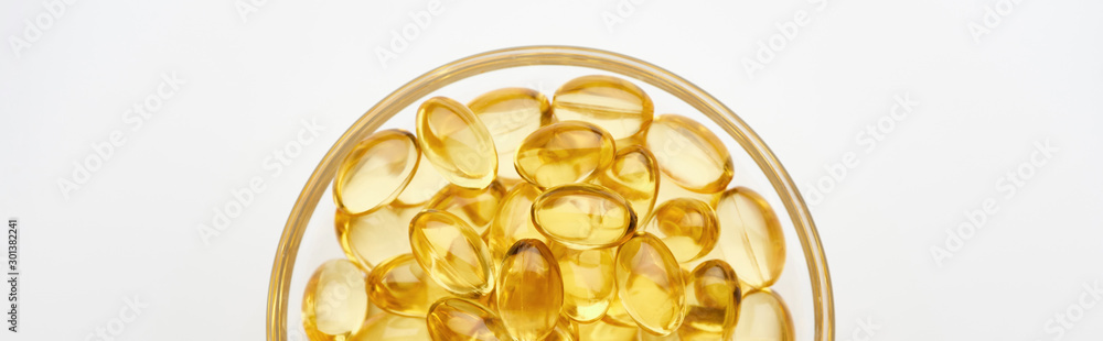 top view of golden fish oil capsules in glass bowl on white background, panoramic shot top view of golden fish oil capsules in glass bowl on white background, panoramic shot