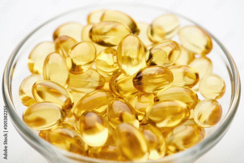 close up view of golden fish oil capsules in glass bowl on white background close up view of golden fish oil capsules in glass bowl on white background