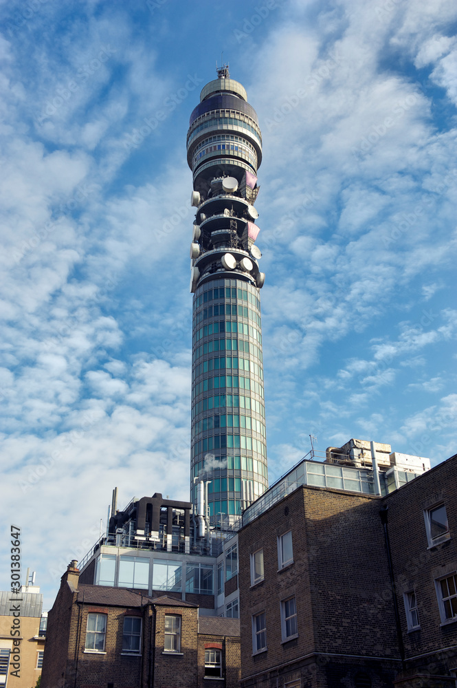 Communications tower decorated with satellite dishes standing outdoors against blue sky in London, UK
