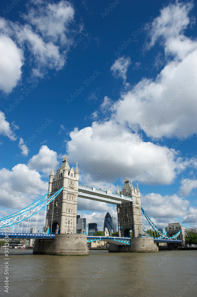 Bright sunny daytime view of Tower Bridge with puffy white clouds above the River Thames in London, UK