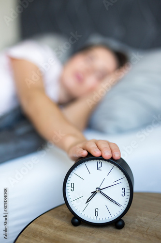Obraz na plátně morning concept - young sleepy woman awaking up with alarm clock in bedroom