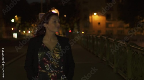 Attractive stylish caucasian modern woman wearing flower dress and black jacket and red hair walking through the street by night in Paris. 4K UHD. Slow Motion.