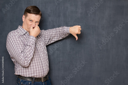 Portrait of dissatisfied man showing thumb down, pinching nose