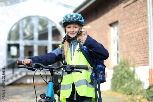 Mädchen mit Fahrradhelm und steht lachend an ihrem Fahrrad und zeigt Daumen hoch