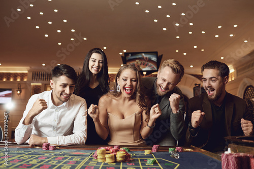Foto Happy people are betting in gambling at roulette poker in a casino