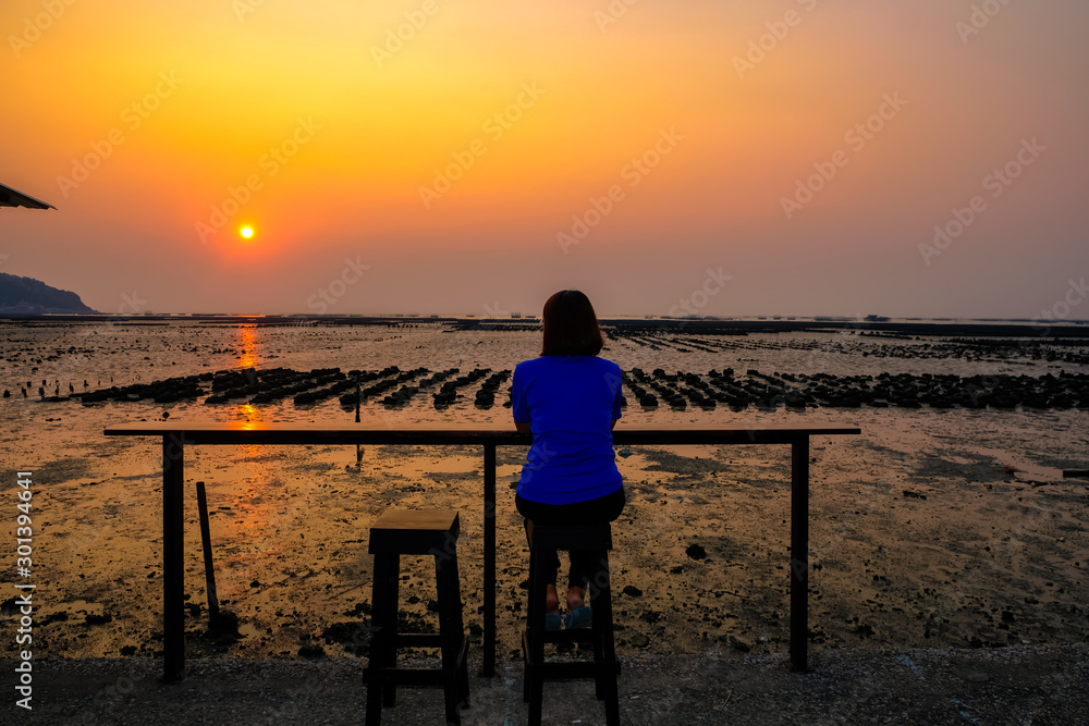 Unidentified woman sitting on the chair with sunset is setting the horizon in the mangrove forest in Pattaya of Thailand.