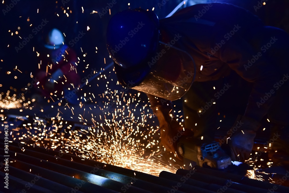 worker cutting steel tube with grider in the drak room. Human working in the confined space. Dark blue tone. worker cutting steel tube with grider in the drak room. Human working in the confined space. Dark blue tone.