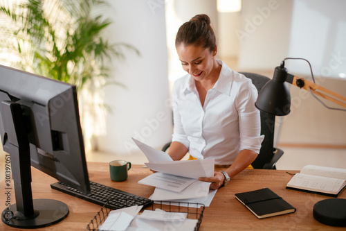 Businesswoman in office. Beautiful young woman working on paperwork at her workplace. © JustLife