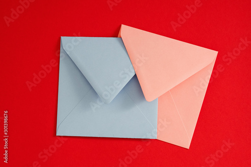 Romantic mail. Flat lay of pale blue and pink blank envelopes on red background. Copy space.
