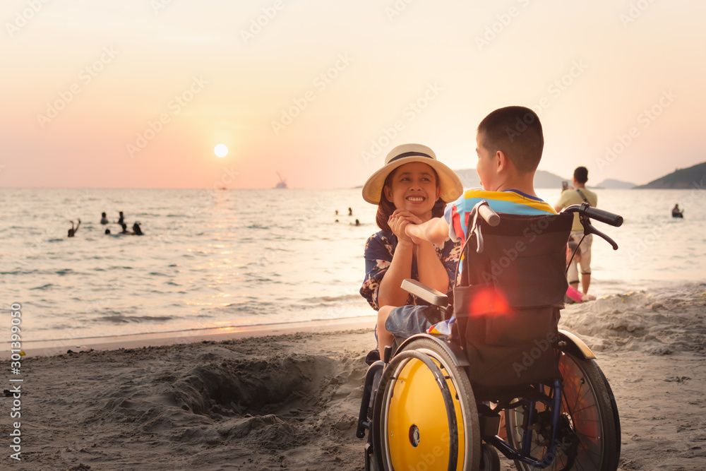 Mother and Asian special child on wheelchair is happily on the beach,Mom and son spend holiday to travel and learning about nature around the sea,Life in the education age, Happy disabled kid concept. - obrazy, fototapety, plakaty 