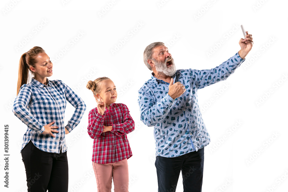Happy family with child looks happy and posing isolated on white studio background. Concept of human emotions, facial expression, good relations. Maling selfie. Grandpa, mother and daughter. Happy family with child looks happy and posing isolated on white studio background. Concept of human emotions, facial expression, good relations. Maling selfie. Grandpa, mother and daughter.