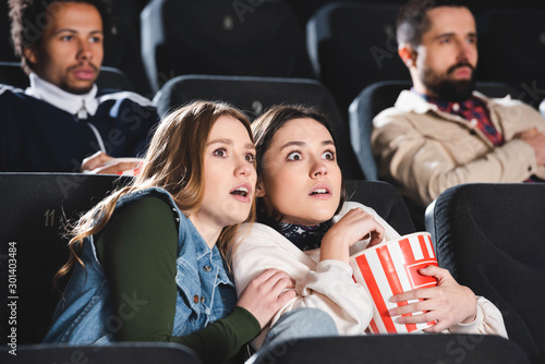 selective focus of scared friends with popcorn watching movie in cinema