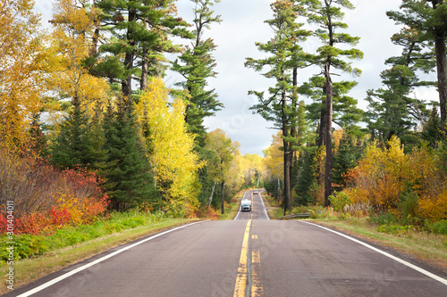 Camper and pickup truck drive below tall pines and autumn color on Minnesota's Gunflint Trail photo