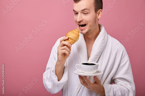 A perky guy in a white bathrobe with croissant